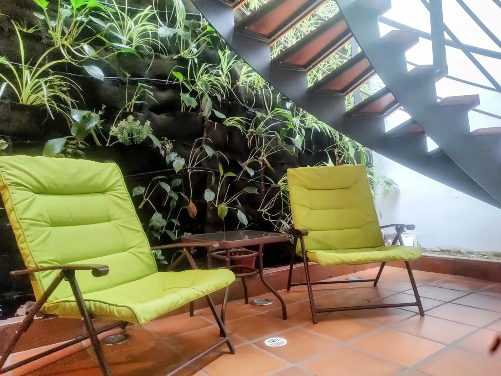 Terraza con jardín vertical y sillas verdes